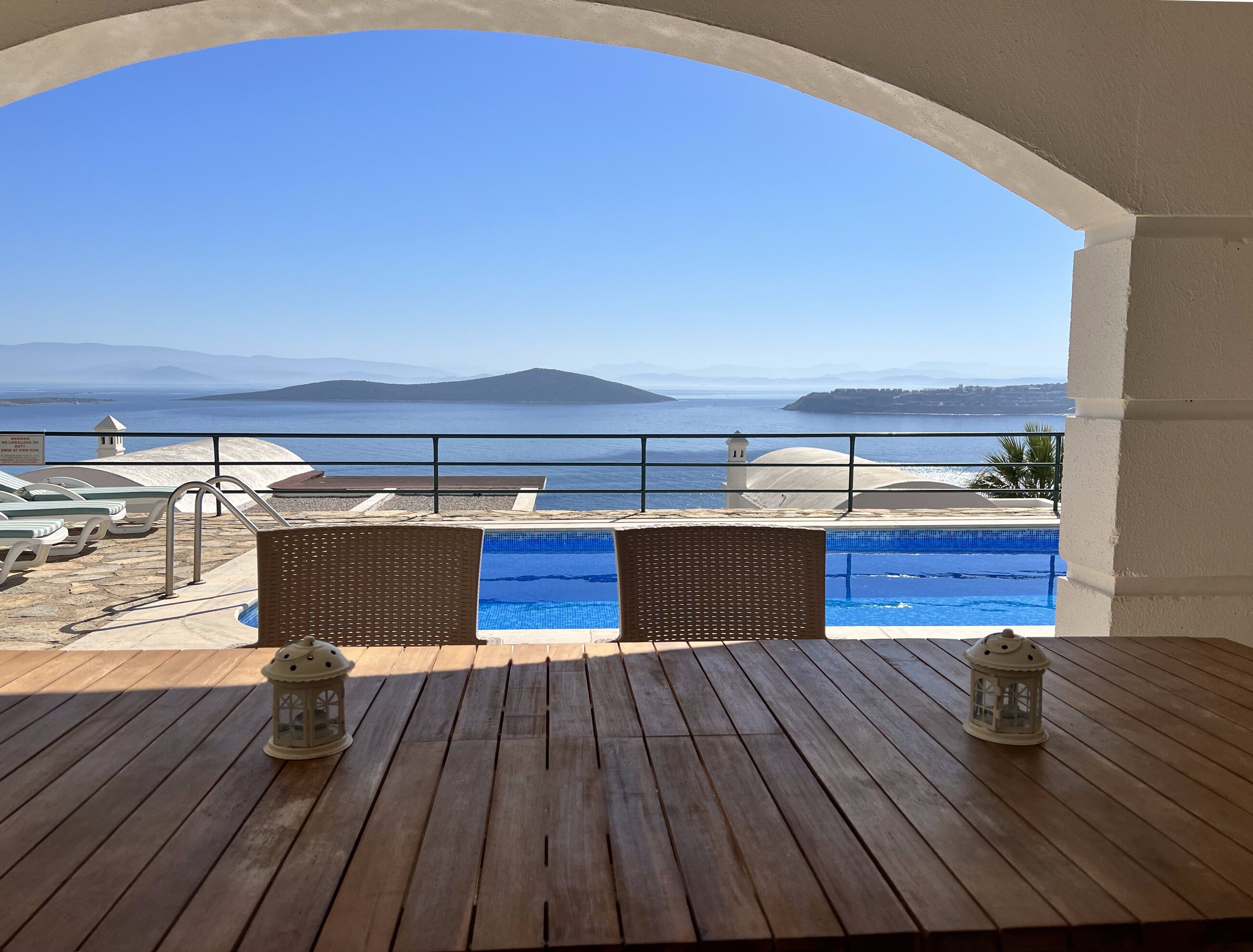 The covered terrace of Villa Mia, framed by a white arch, looking over the private pool to the Aegean and the islands of Gündoğan bay